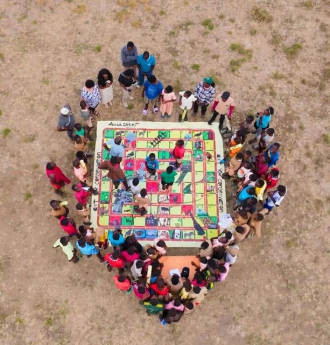 Overhead view of a crowd of people gathered around a giant educational board game on the ground.